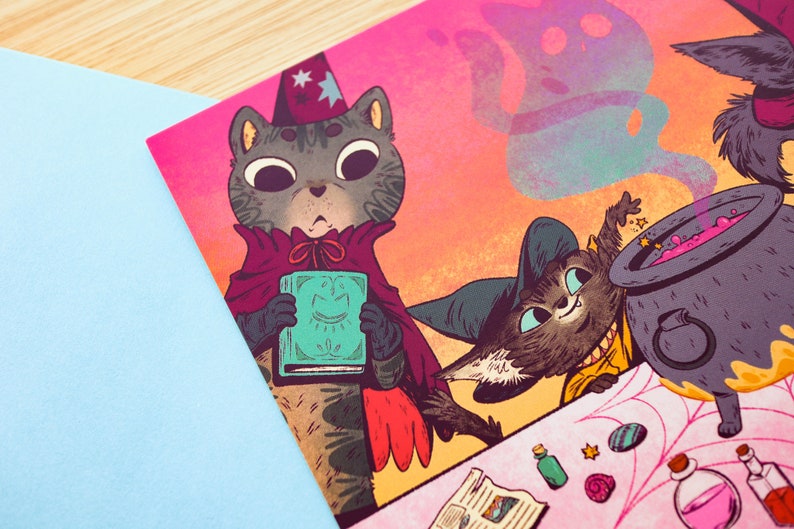 May include: Two cats dressed as witches are making a potion in a cauldron. One cat is holding a book with a smiling face on the cover. The other cat is stirring the cauldron with a wand. The cauldron is filled with pink liquid and there are stars and smoke coming out of it.