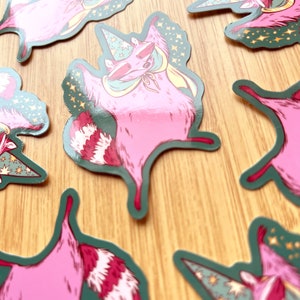 May include: A set of five pink raccoon stickers with a green background and stars. Each raccoon is wearing a wizard hat and has a pink and white striped tail.