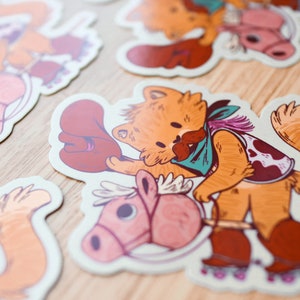 May include: A sticker featuring a cartoon cat wearing a cowboy hat and bandana, riding a pink rocking horse. The cat has a brown and white cow print vest and brown boots. The sticker has a white background.