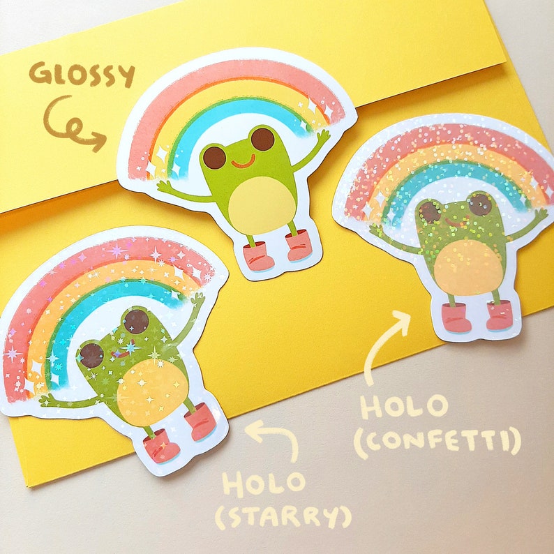 May include: Three frog stickers with rainbow arches. The top sticker is glossy, the middle sticker is holographic with a starry effect, and the bottom sticker is holographic with a confetti effect. The stickers feature the text "HOLO (STARRY)" and "HOLO (CONFETTI)".