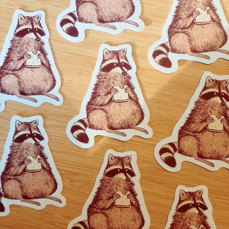 May include: Set of ten illustrated stickers featuring raccoons eating sandwiches. The raccoons are depicted in a cartoon style with brown fur, black masks, and white bellies. The stickers are printed on white, glossy paper and have a rounded rectangular shape.
