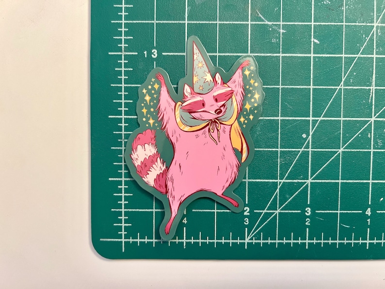 May include: A pink raccoon wearing a blue and white pointed hat with a yellow cape and stars around it. The raccoon is standing on its hind legs with its arms raised in the air.