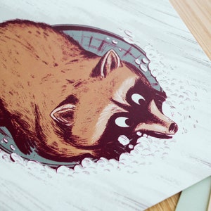 May include: A cartoon illustration of a raccoon peeking out of a sewer drain with a surprised expression. The raccoon is brown with a black tail and white fur around its eyes. The drain is grey and has a white rim. The background is white with a wood grain texture.