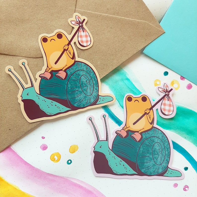 May include: Two stickers featuring a frog riding a snail. The first sticker has a yellow frog with a red and white checkered bag on a green snail with a brown shell. The second sticker has an orange frog with a red and white checkered bag on a green snail with a blue shell.