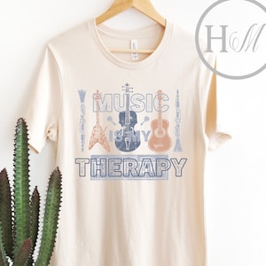 Pode incluir: Uma camiseta bege com o texto "Music is my therapy" estampado na frente. O texto &eacute; cercado por imagens de instrumentos musicais, incluindo uma guitarra, um violino, um clarinete e bateria.