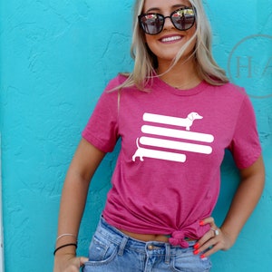 May include: A pink t-shirt with a white graphic of a dachshund dog on top of three white stripes.
