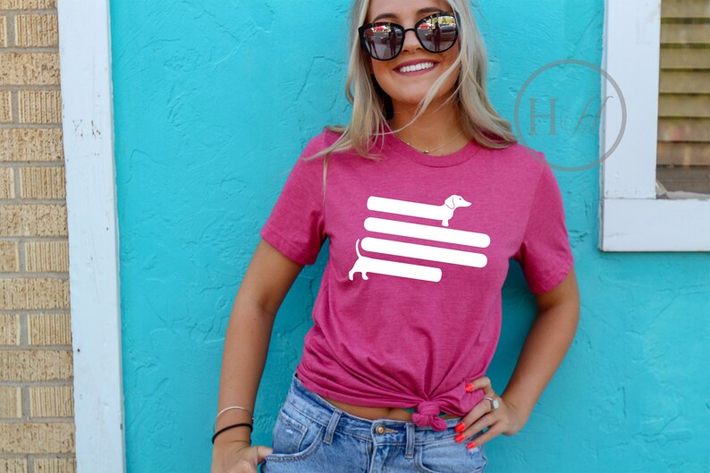 May include: A pink t-shirt with a white graphic of a dachshund dog on top of three white stripes.