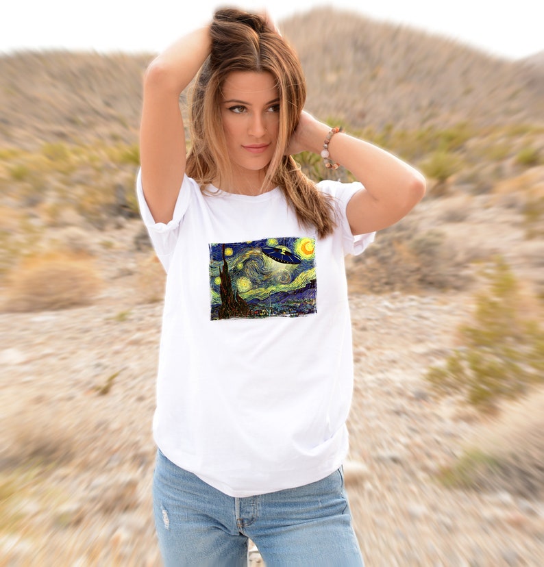 May include: White t-shirt with a graphic print of Vincent van Gogh's Starry Night with a UFO flying over the town.