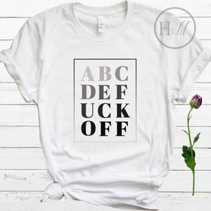 May include: White t-shirt with a black and gray graphic that says "ABC DEF UCK OFF" in a blocky font.
