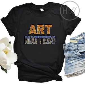 May include: Black t-shirt with the text "ART MATTERS" in colorful letters. The letters are made up of a floral pattern.