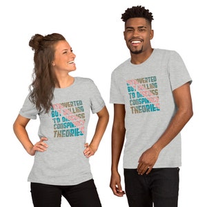 May include: Two people wearing gray t-shirts with the text "Introverted but willing to discuss conspiracy theories" printed in a colorful, layered font.