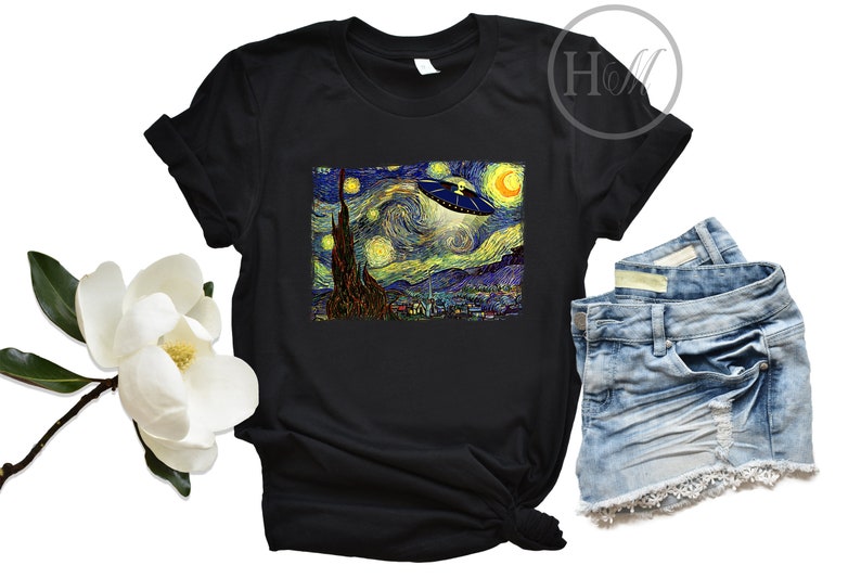 May include: A black t-shirt with a graphic print of Vincent van Gogh's Starry Night with a UFO flying over the town. The t-shirt is laying on a white surface with a pair of blue denim shorts.
