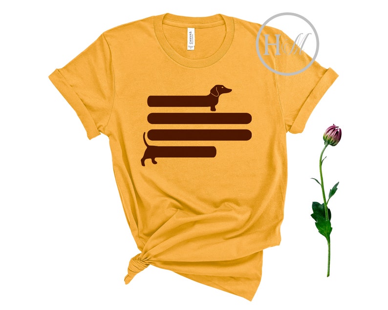 May include: A yellow t-shirt with a brown dachshund silhouette design. The dachshund is depicted walking across four horizontal lines.