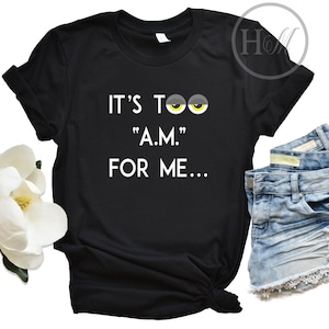 May include: Black t-shirt with white text that reads "It's too "A.M." for me..." with two cartoon eyes above the text.