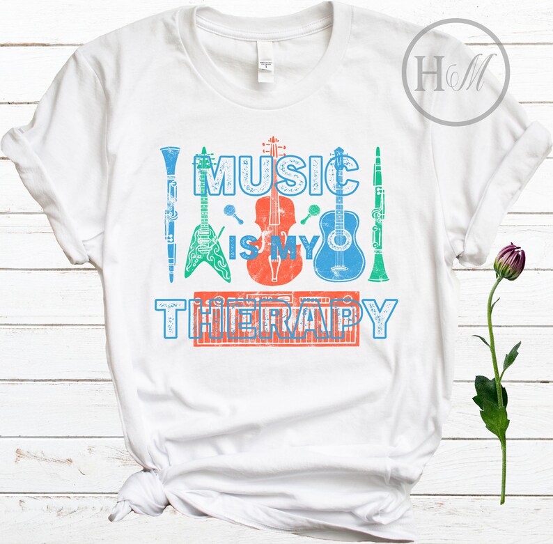Pode incluir: Camiseta branca com o texto "Music is my therapy" impresso em azul, vermelho e verde. O texto &eacute; cercado por imagens de instrumentos musicais, incluindo uma guitarra, um violino, um clarinete e um teclado.