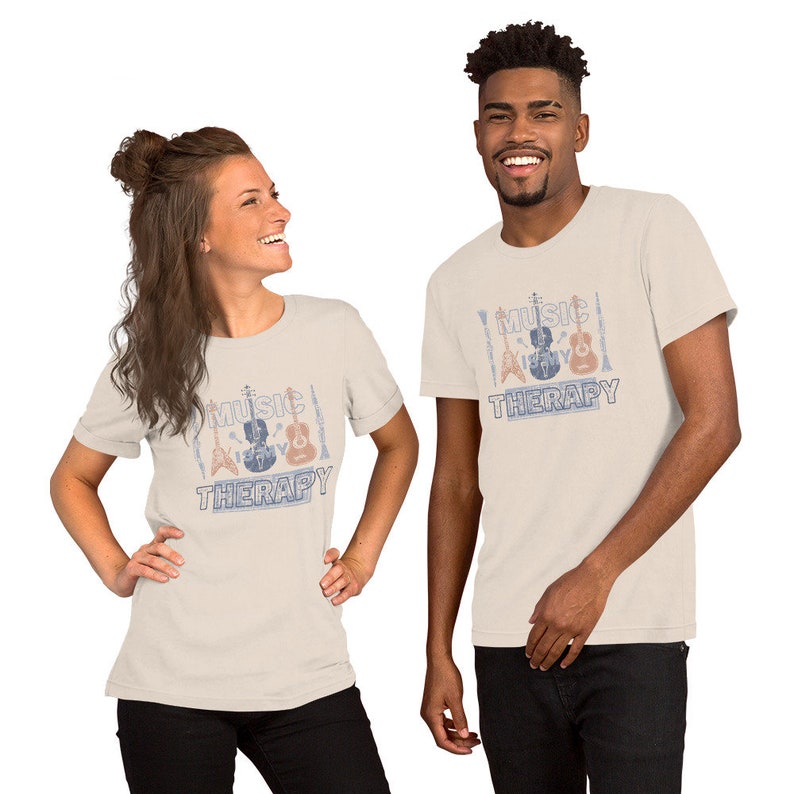 Pode incluir: Duas pessoas vestindo camisetas bege com um gr&aacute;fico de estilo vintage de instrumentos musicais e o texto "Music Therapy".