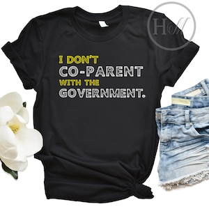 May include: Black t-shirt with the text "I don't co-parent with the government." in white and yellow lettering.