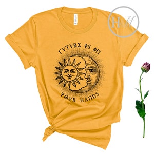 May include: A mustard yellow t-shirt with a black sun and moon graphic and the text "ΓΥΝΤΥΡΕΣ ΦΣ ΦΠ YOUR HANDS".