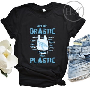 Puede incluir: Camiseta negra con un gráfico azul de una tortuga marina atrapada en una bolsa de plástico. El texto "Let's get drastic about plastic" está impreso en la camiseta.