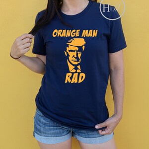 May include: A navy blue t-shirt with a yellow graphic of a person's face and the text "Orange Man Rad".