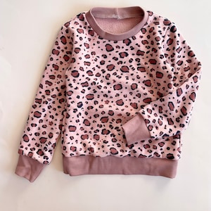 Puede incluir: Una sudadera rosa de manga larga con estampado de leopardo marrón y negro.