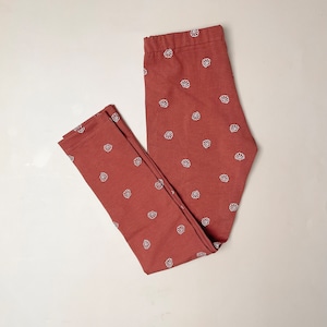 Puede incluir: Un par de leggings de color óxido con un patrón de conchas blancas.