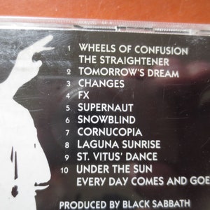 May include: Black and white CD case with a tracklist for the album "Wheels of Confusion" by Black Sabbath. The tracklist includes "Wheels of Confusion", "The Straightener", "Tomorrow's Dream", "Changes", "FX", "Supernaut", "Snowblind", "Cornucopia", "Laguna Sunrise", "St. Vitus' Dance", "Under the Sun", and "Every Day Comes and Goes".