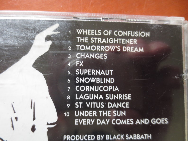 May include: Black and white CD case with a tracklist for the album "Wheels of Confusion" by Black Sabbath. The tracklist includes "Wheels of Confusion", "The Straightener", "Tomorrow's Dream", "Changes", "FX", "Supernaut", "Snowblind", "Cornucopia", "Laguna Sunrise", "St. Vitus' Dance", "Under the Sun", and "Every Day Comes and Goes".