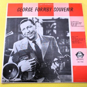 Puede incluir: Una foto en blanco y negro de George Formby sosteniendo un banjo. La foto está en una funda de disco roja, blanca y negra con el texto "George Formby Souvenir" en letras blancas. La funda del disco también incluye el texto "Ace of Clubs London ACL 7906".