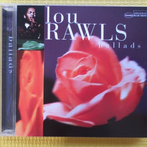 Puede incluir: Una caja de CD con una rosa roja en la parte delantera. El título del álbum es "Lou Rawls Ballads" y el artista es Lou Rawls. La caja del CD es negra con una columna vertebral plateada.
