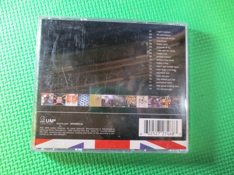 Puede incluir: Una caja de CD con fondo negro y borde blanco. La parte delantera de la caja presenta una foto de una banda. La parte posterior de la caja enumera las canciones del CD, incluyendo "I Can't Explain", "Magic Bus", "Pinball Wizard", "Behind Blue Eyes", "Won't Get Fooled Again", "Love Reign O'er Me", "Squeeze Box", "Who Are You", "You Better You Bet", "Eminence Front", "Real Good Looking Boy", y "It's Not Enough". La caja tambi&eacute;n incluye un c&oacute;digo de barras y el texto "GUM" y "thesho.com GETMUSICCA".
