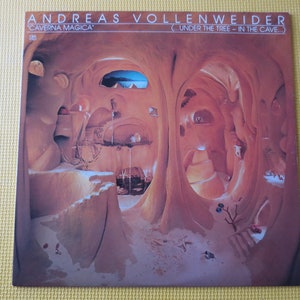 May include: A record album cover featuring a cave-like interior with a sandy floor and a small tree in the foreground. The album title "Caverna Magica" and the artist's name "Andreas Vollenweider" are printed on the cover.