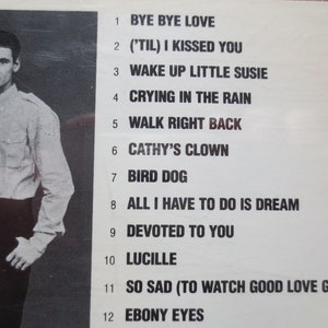 May include: A black and white photograph of a band with a list of 12 song titles. The band members are wearing casual clothing. The song titles include "Bye Bye Love", "('Til) I Kissed You", "Wake Up Little Susie", "Crying In The Rain", "Walk Right Back", "Cathy's Clown", "Bird Dog", "All I Have To Do Is Dream", "Devoted To You", "Lucille", "So Sad (To Watch Good Love Go Bad)", and "Ebony Eyes".
