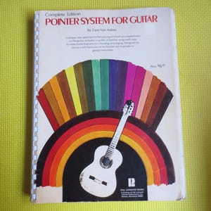 May include: A book titled "Complete Edition Pointer System for Guitar" by Zane Van Auken. The cover features a rainbow design with a guitar in the center. The price is $6.95.