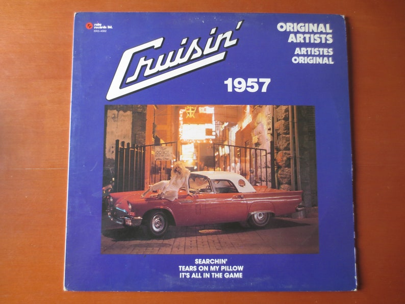 Pu&ograve; includere: Una copertina di un album di vinile vintage con una Ford Thunderbird rossa convertibile del 1957 con una donna in un abito bianco seduta sul cofano. La copertina dell'album &egrave; blu con testo bianco che recita "Cruisin' 1957", "Original Artists", "Artistes Original", "Searchin'", "Tears on My Pillow", e "It's All in the Game".