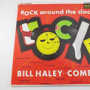 May include: A red, black, and yellow vinyl record cover with the title "ROCK around the clock" and the artist "BILL HALEY-COMETS". The cover features a clock face with a smiling face and a sock with stripes.