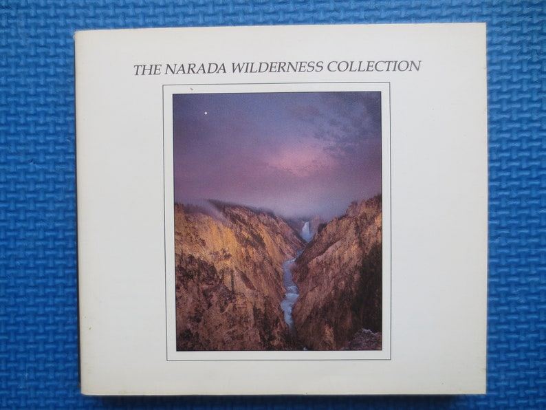 May include: The Narada Wilderness Collection album cover features a photograph of a canyon with a river flowing through it. The sky is a vibrant purple and pink, with a single star visible in the upper left corner.