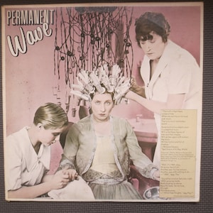 May include: A vintage record album cover featuring a woman getting a permanent wave at a salon. The woman is sitting in a chair with curlers in her hair, while a stylist works on her hair. The album cover is pink and white and features the text "Permanent Wave".