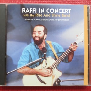以下が含まれることがあります： ギターを弾いている男性の写真が写っているCDケース。ケースには「Raffi in Concert with the Rise And Shine Band. From the video soundtrack of the live performance.」という文字が書かれている