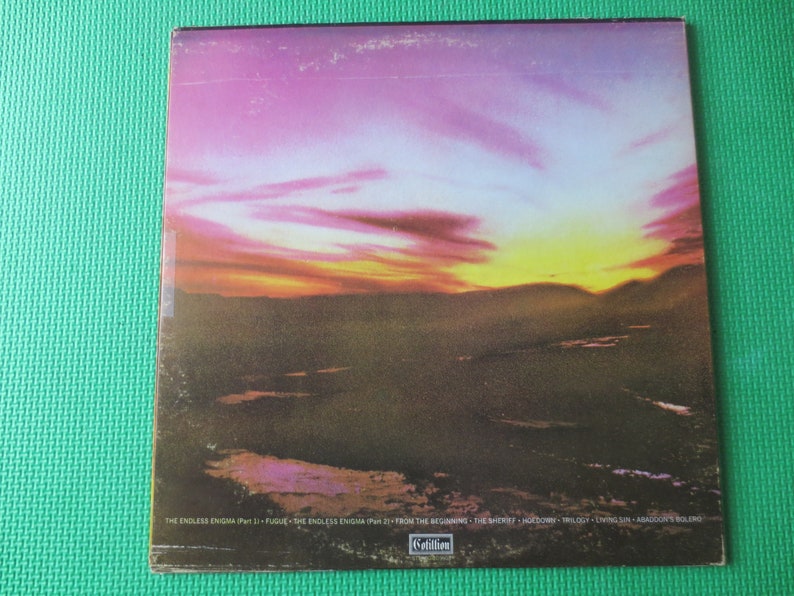May include: A vintage vinyl record album cover with a sunset over a landscape. The album title is "The Endless Enigma" and the track list includes "From The Beginning", "The Shorey", "Hodow", "Trilogy", "Crystal Sun", and "Armageddon's Bolero".