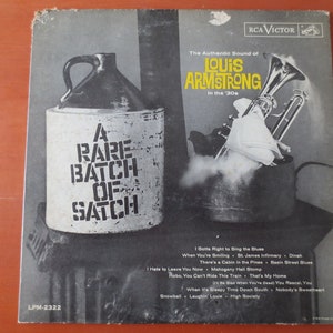 May include: A black and white album cover with a vintage design. The cover features a jug with the text "A Rare Batch of Satch" and a trumpet with smoke coming out of it. The album title is "The Authentic Sound of Louis Armstrong in the '30s". The album is titled "A Rare Batch of Satch" and features a list of songs on the back cover.
