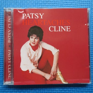 Puede incluir: Una caja de CD roja con una foto de Patsy Cline en la portada. El texto en la caja dice "Patsy Cline Heartaches".