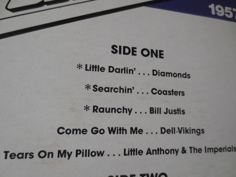 Pu&ograve; includere: Una copertina di un album di vinile vintage con il titolo "SIDE ONE" e un elenco di canzoni, tra cui "Little Darlin'" dei Diamonds, "Searchin'" dei Coasters, "Raunchy" di Bill Justis, "Come Go With Me" dei Dell-Vikings e "Tears On My Pillow" di Little Anthony & The Imperials. La copertina dell'album include anche l'anno "1957".