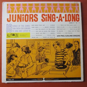 Pode incluir: Uma capa de álbum de vinil vintage com um grupo de crianças cantando junto a um toca-discos. A capa do álbum é amarela com uma ilustração em preto e branco das crianças em uma sala de aula. O título do álbum é "Juniors Sing-A-Long" com o texto "16 Songs of the Christian Faith for Juniors to Sing and Listen To" e "with Paul Sjolund Singers".