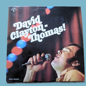 Peut inclure: Pochette d'album vinyle vintage avec David Clayton-Thomas. Le nom de l'artiste est en grandes lettres blanches. L'image montre l'artiste chantant dans un microphone avec un fond rouge et bleu.