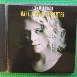 May include: A CD case with a black background and a photo of a woman with blonde hair. The text "Come On Come On" and "MARY-CHAPIN CARPENTER" is printed in yellow on the case.