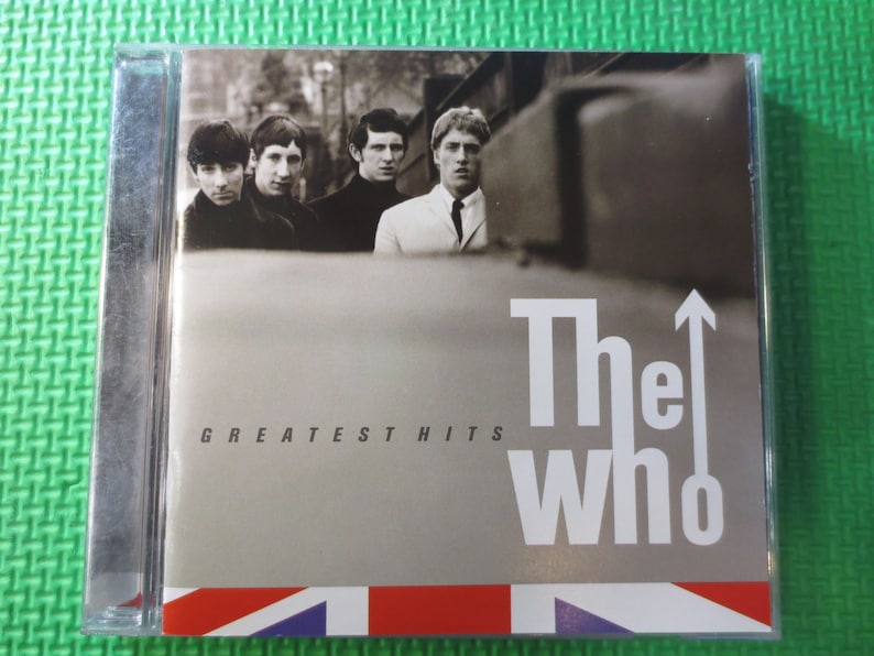 Puede incluir: Una caja de CD plateada con una foto en blanco y negro de los miembros de la banda The Who. El texto "The Who" y "Greatest Hits" est&aacute; impreso en la parte delantera de la caja.
