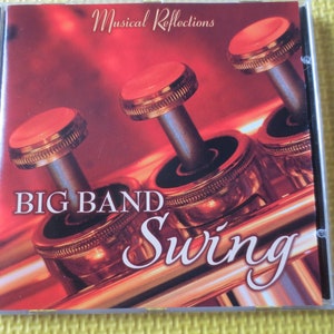 Puede incluir: Una caja de CD con un fondo rojo y una trompeta dorada con el texto "Musical Reflections Big Band Swing" en la parte delantera.