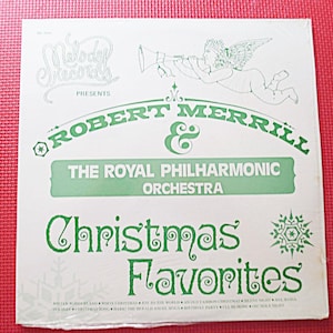 May include: A white vinyl record album cover with green text that reads "Merry Christmas Presents Robert Merrill & The Royal Philharmonic Orchestra Christmas Favorites". The cover features a cartoon angel playing a trumpet.