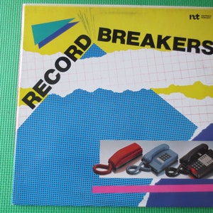 Pode incluir: Uma capa de álbum de vinil amarela, azul e branca com o texto "RECORD BREAKERS" em letras pretas. A capa apresenta três telefones de cores diferentes com fios.